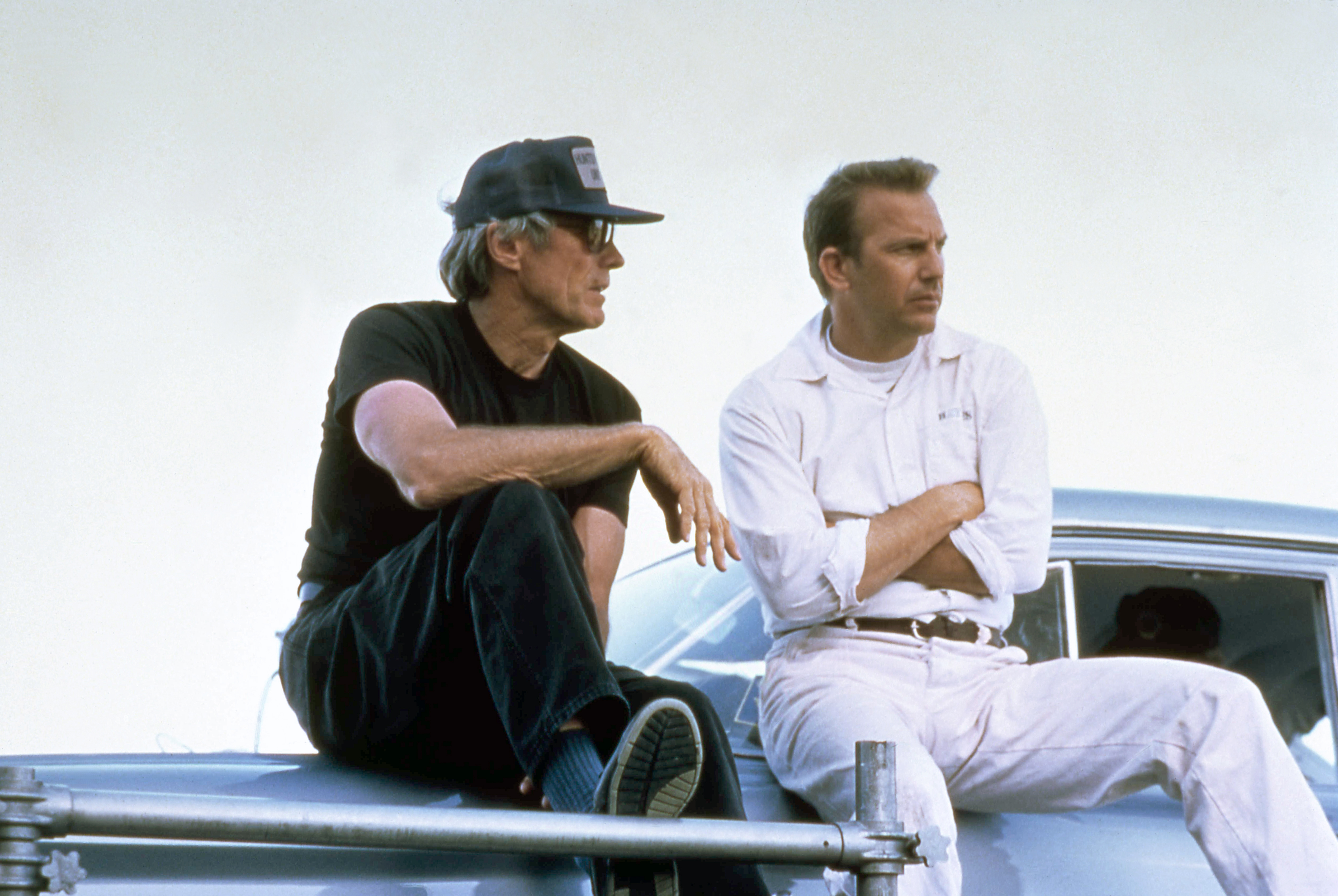 Clint Eastwood and Kevin Costner sitting on a car on the set of the movie