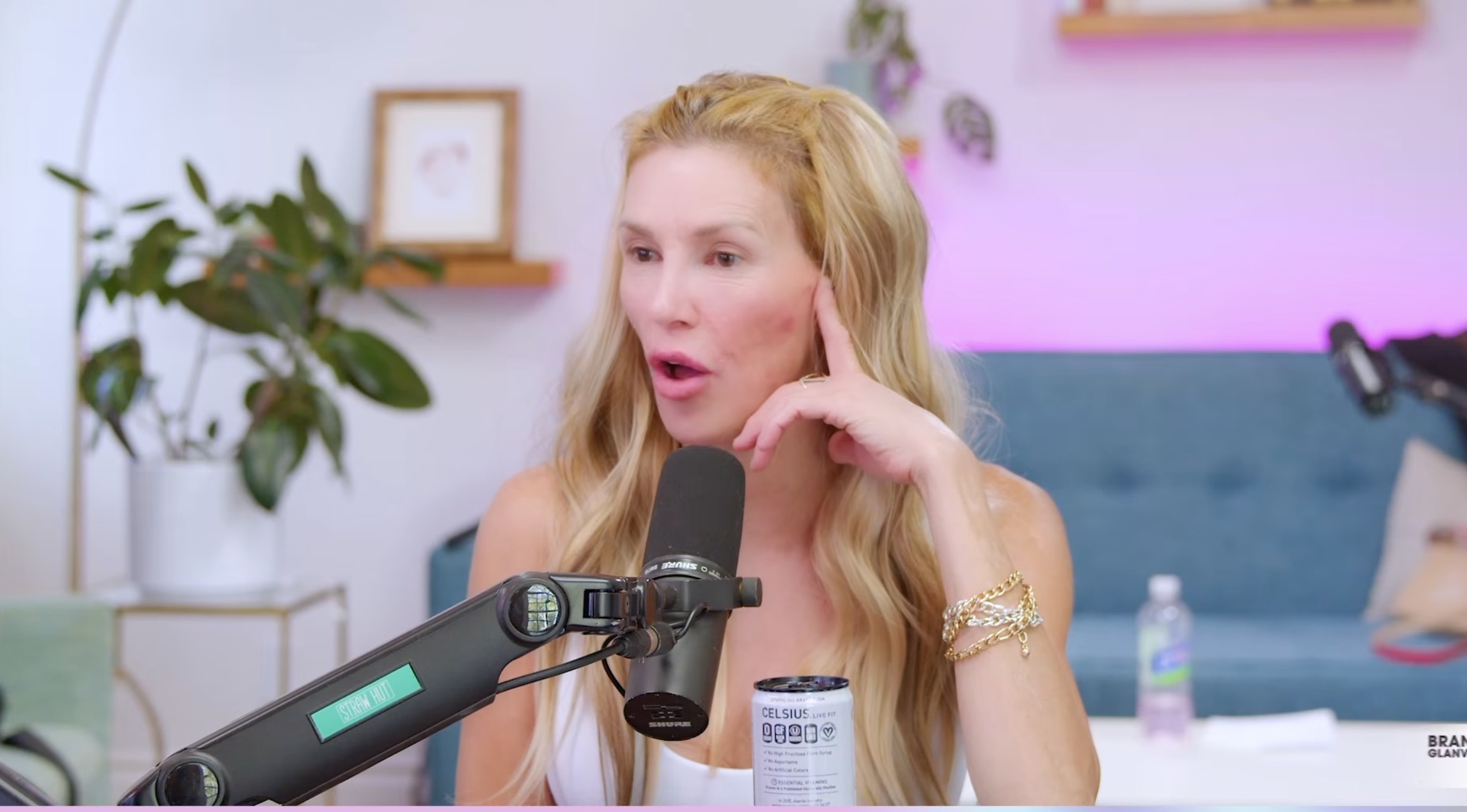 Brandi Glanville with an open mouth and hand near her face, next to a microphone and a "Celsius" branded drink.
