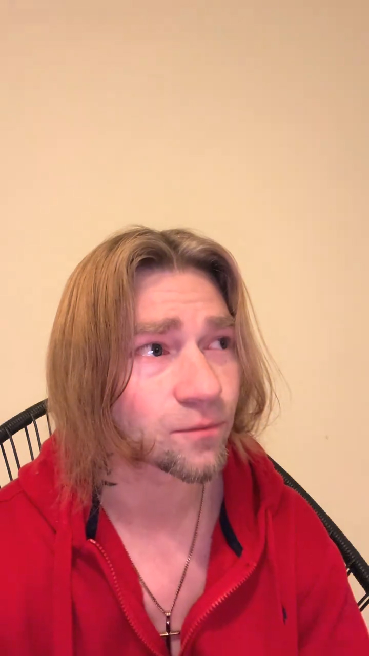Bear Brown, star of Alaskan Bush People, looking to the side with watery eyes, wearing a red hoodie and a cross necklace.
