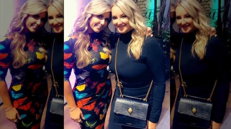 Brandi Passante smiles with her arm around her friend wearing a black dress with colorful butterflies
