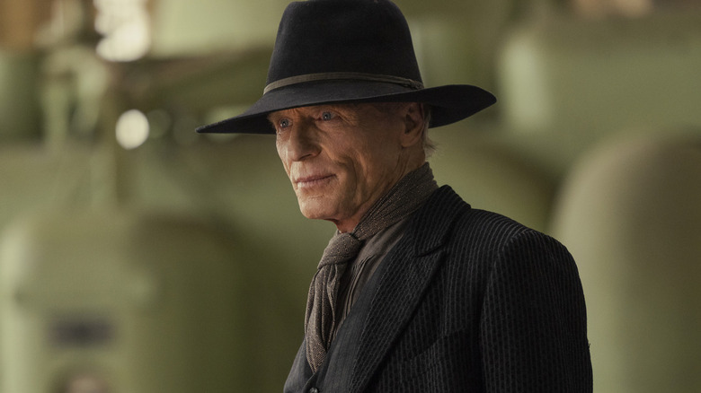 The Man in Black wearing a black suit and cowboy hat standing in front of green machinery in Westworld