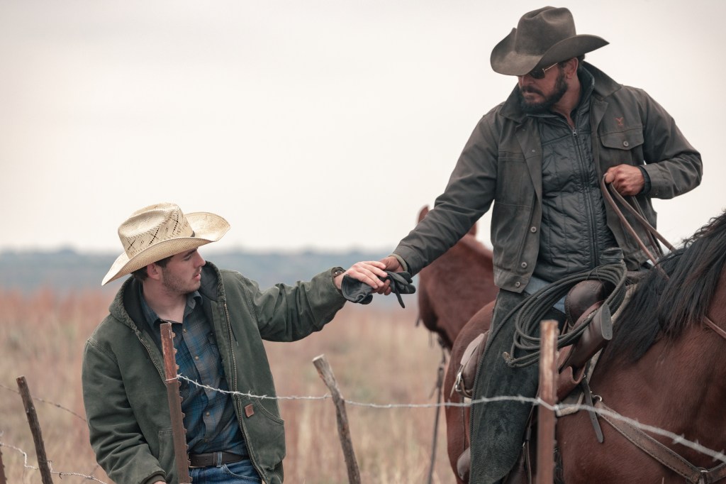 Finn Little as Carter reaching up to take gloves from Cole Hauser as Rip Wheeler on horseback.