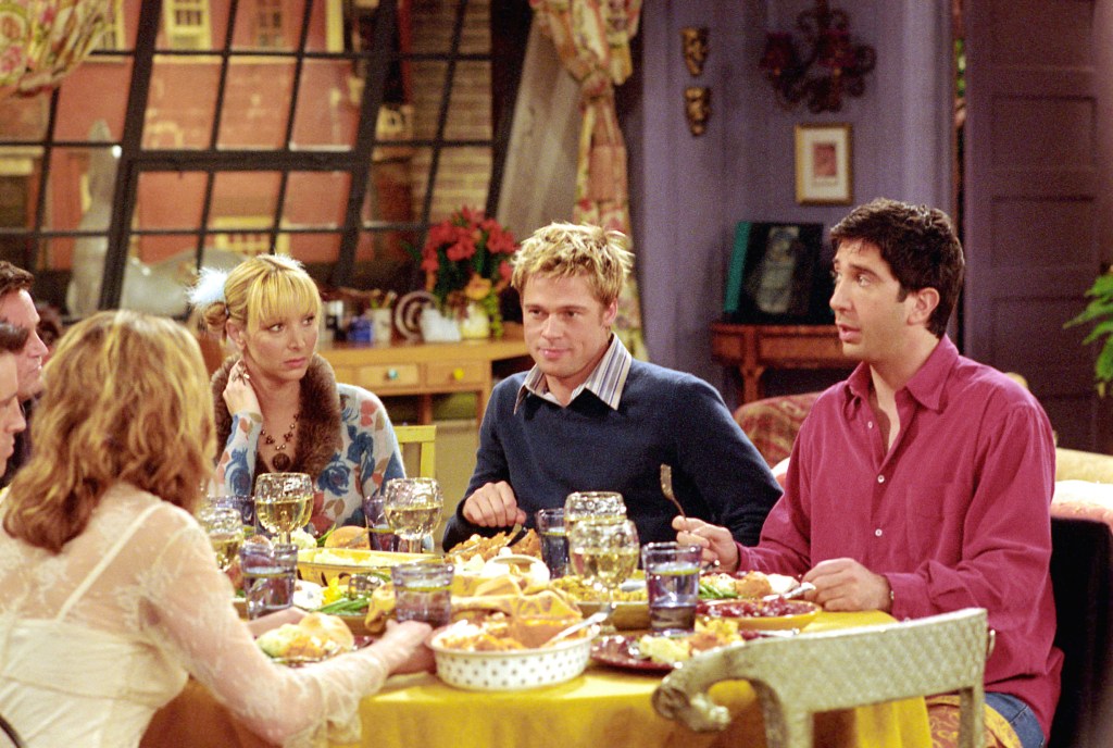 Friends characters Lisa Kudrow, Brad Pitt, and David Schwimmer sitting around a dinner table for Thanksgiving.